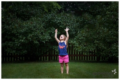 Photograph of young child reaching up to feel summer rain drops and bright sunlight through the clouds. Naperville lifestyle photography