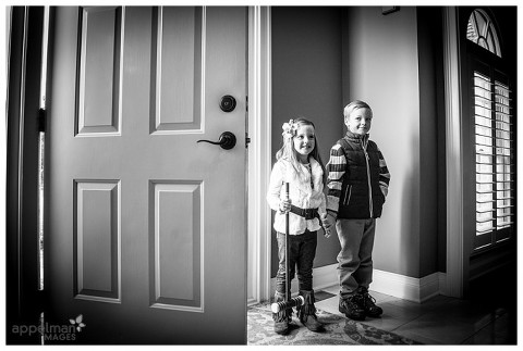 Dramatic black and white of young siblings posing by family door for in home portrait