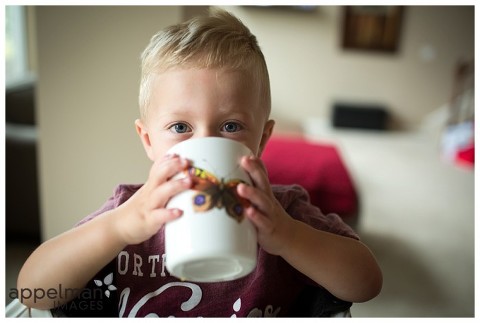 butterfly cup and stormy blue eyes little blonde boy drinking from big cup at home in lifestyle photography session by naperville oswego chicago IL photographer