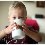 butterfly cup and stormy blue eyes little blonde boy drinking from big cup at home in lifestyle photography session by naperville oswego chicago IL photographer